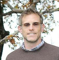A man in glasses and sweater standing next to tree.